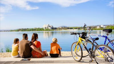Family sitting on waters edge in Canberra with bikes from Cycle Canberra