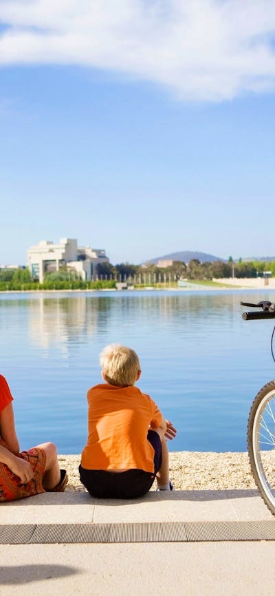 Family sitting on waters edge in Canberra with bikes from Cycle Canberra