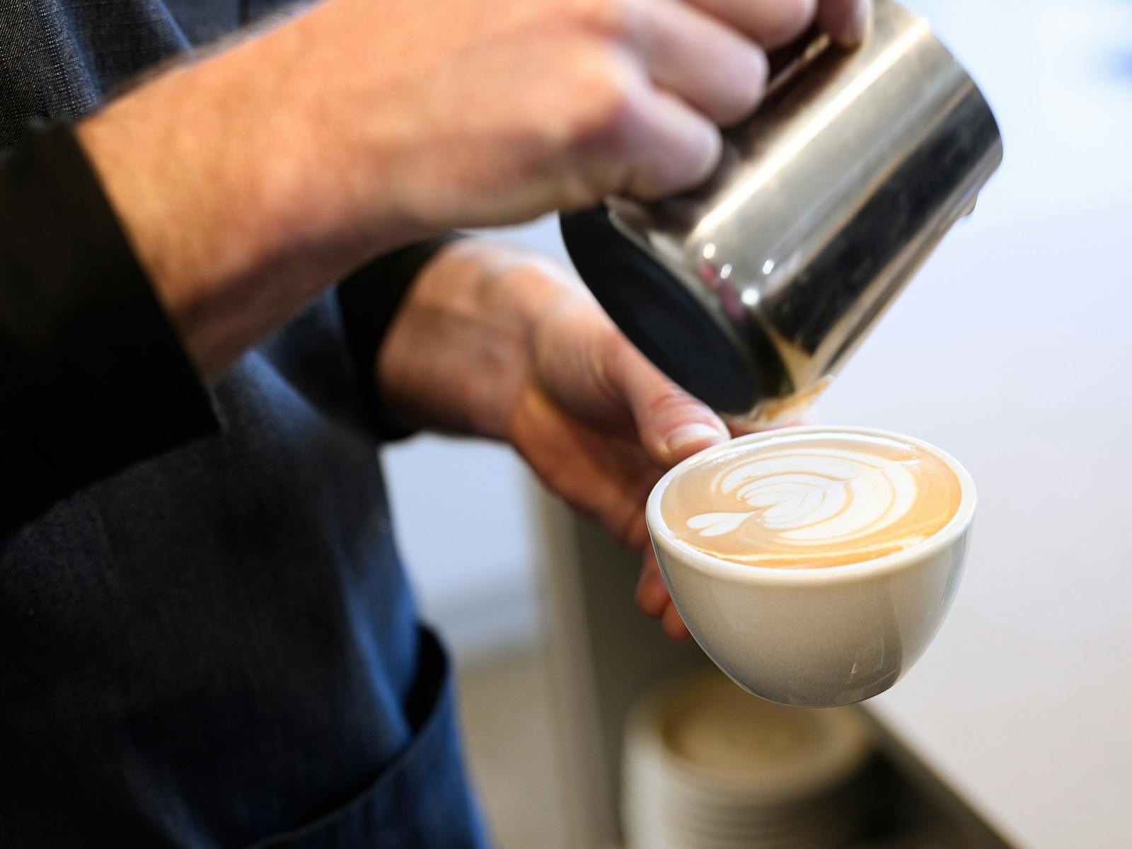 Baristaholding metal milke pitcher and pouring latte art tulip into a small cream cup.