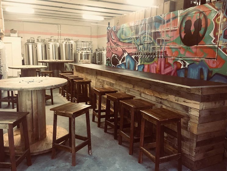 Wooden tables and bar with brewing tanks and graffiti mural behind