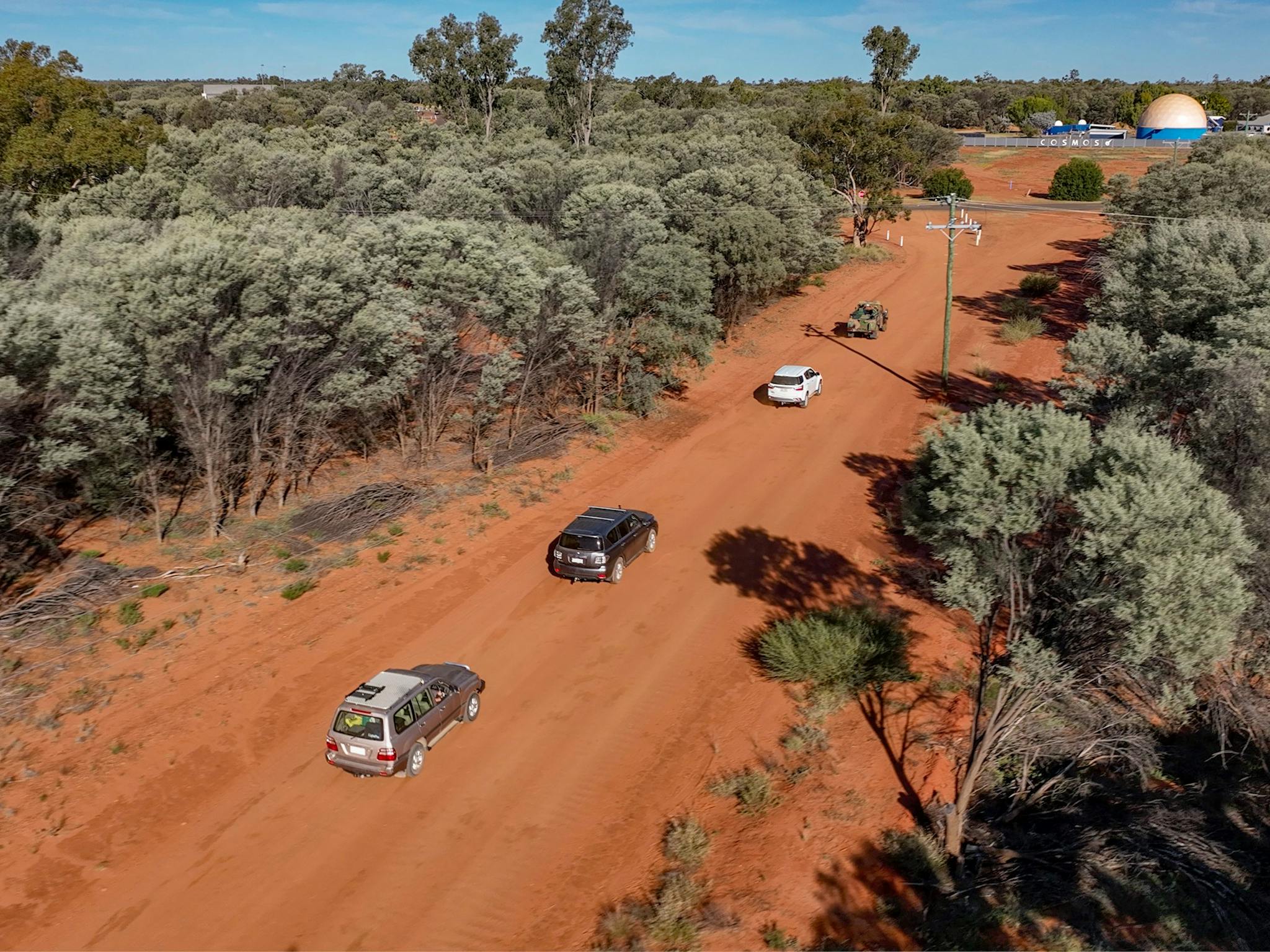 a convoy of cars travelling on a dirt road surrounded by Mulga country a convoy of cars travelling on a dirt road surrounded by Mulga country