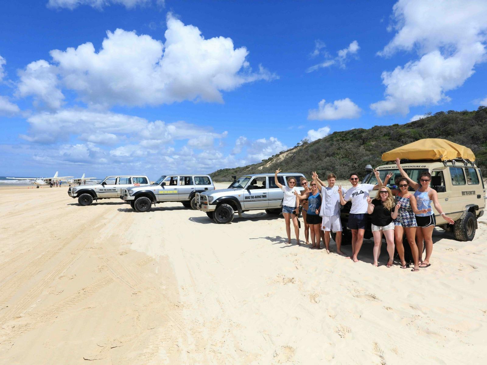 Group of travellers posing beside 4WD vehicles on K'gari Fraser Island beach