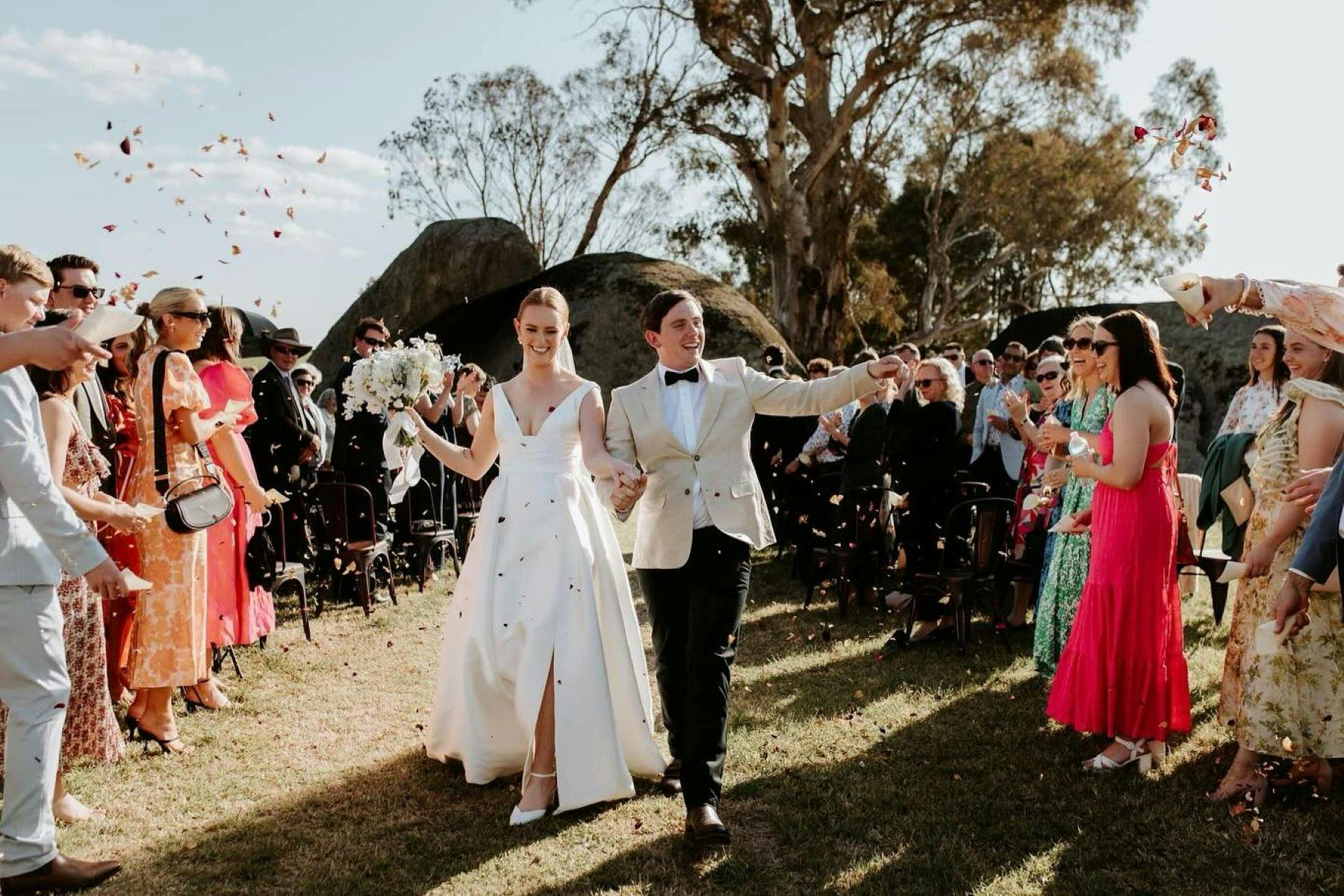 Groom and bride walking down isle together as guests toss petals.