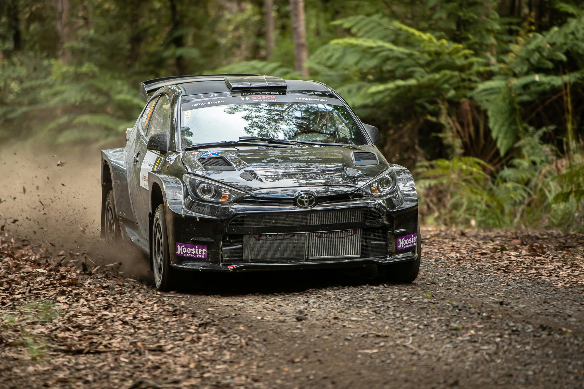 A black rally car driving through the forest