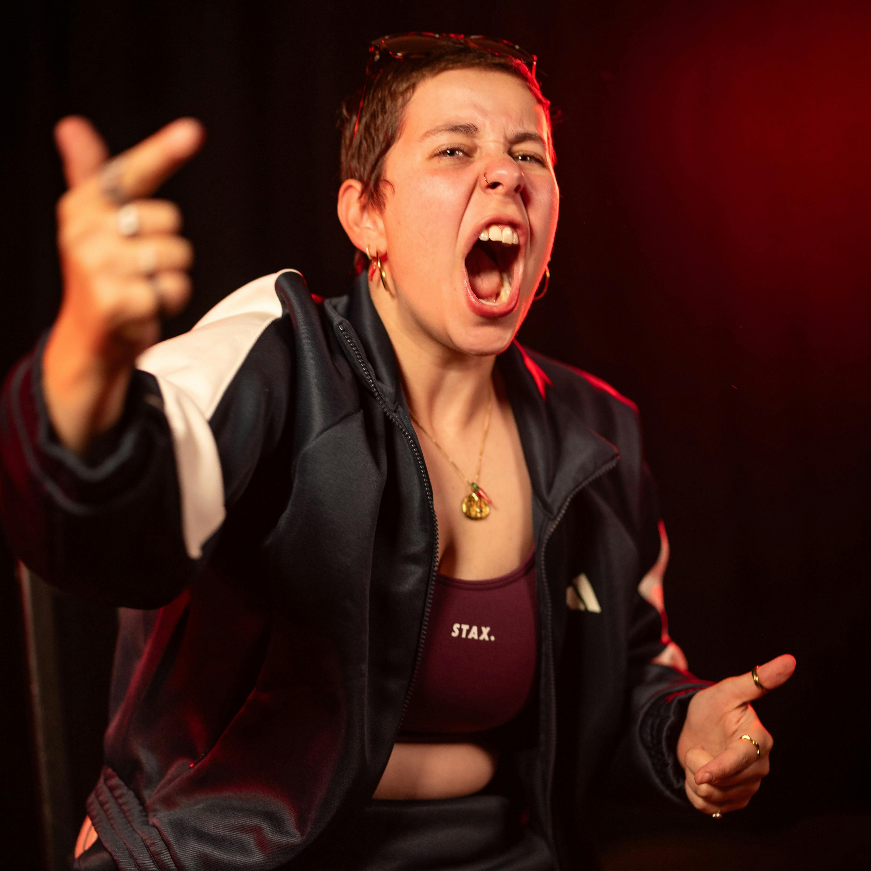 Katherine Sortini, a white woman with short brown hair, points energetically at the camera with both
