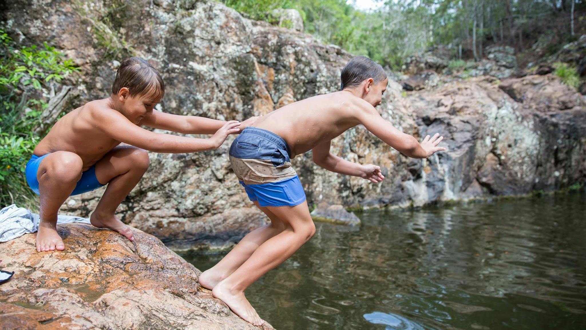 Two young boys jumping into swimming hole off rocks