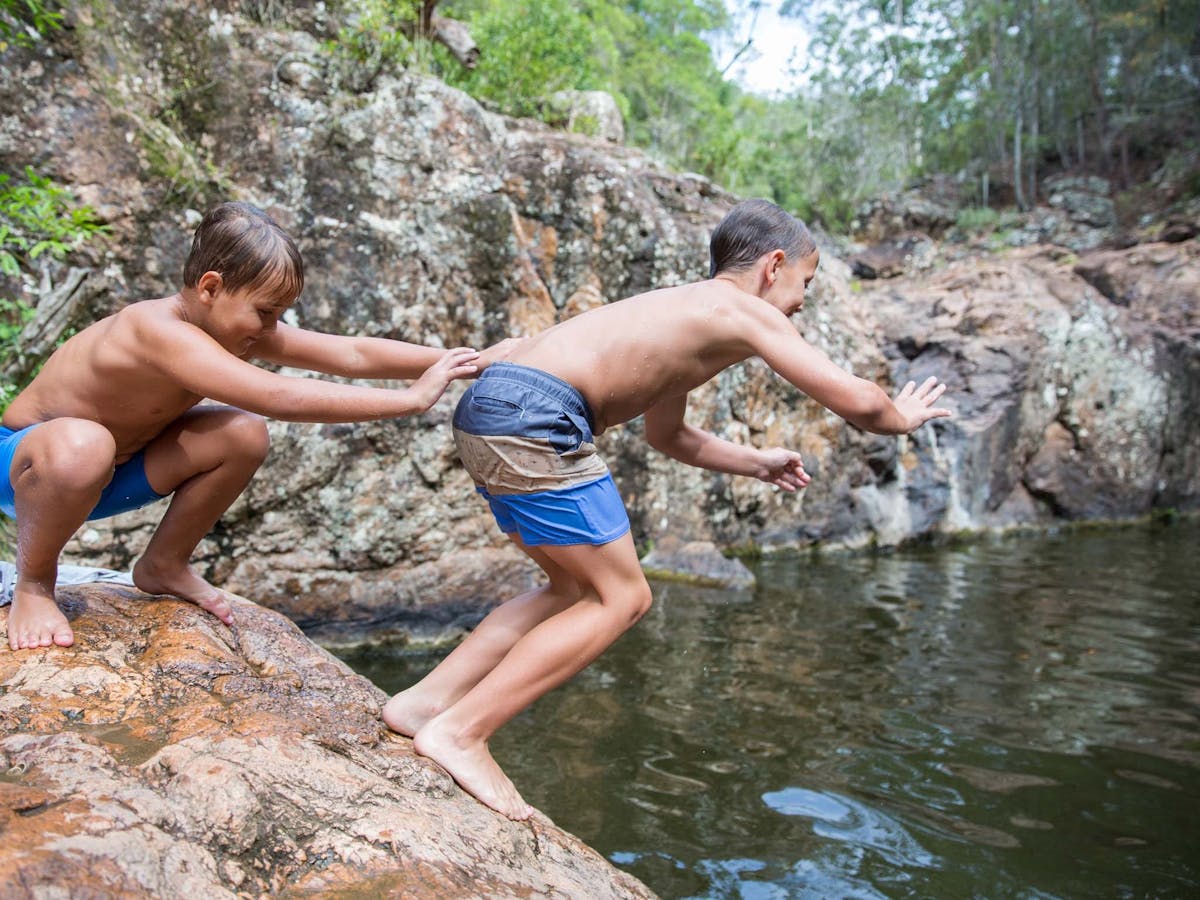 Two young boys jumping into swimming hole off rocks