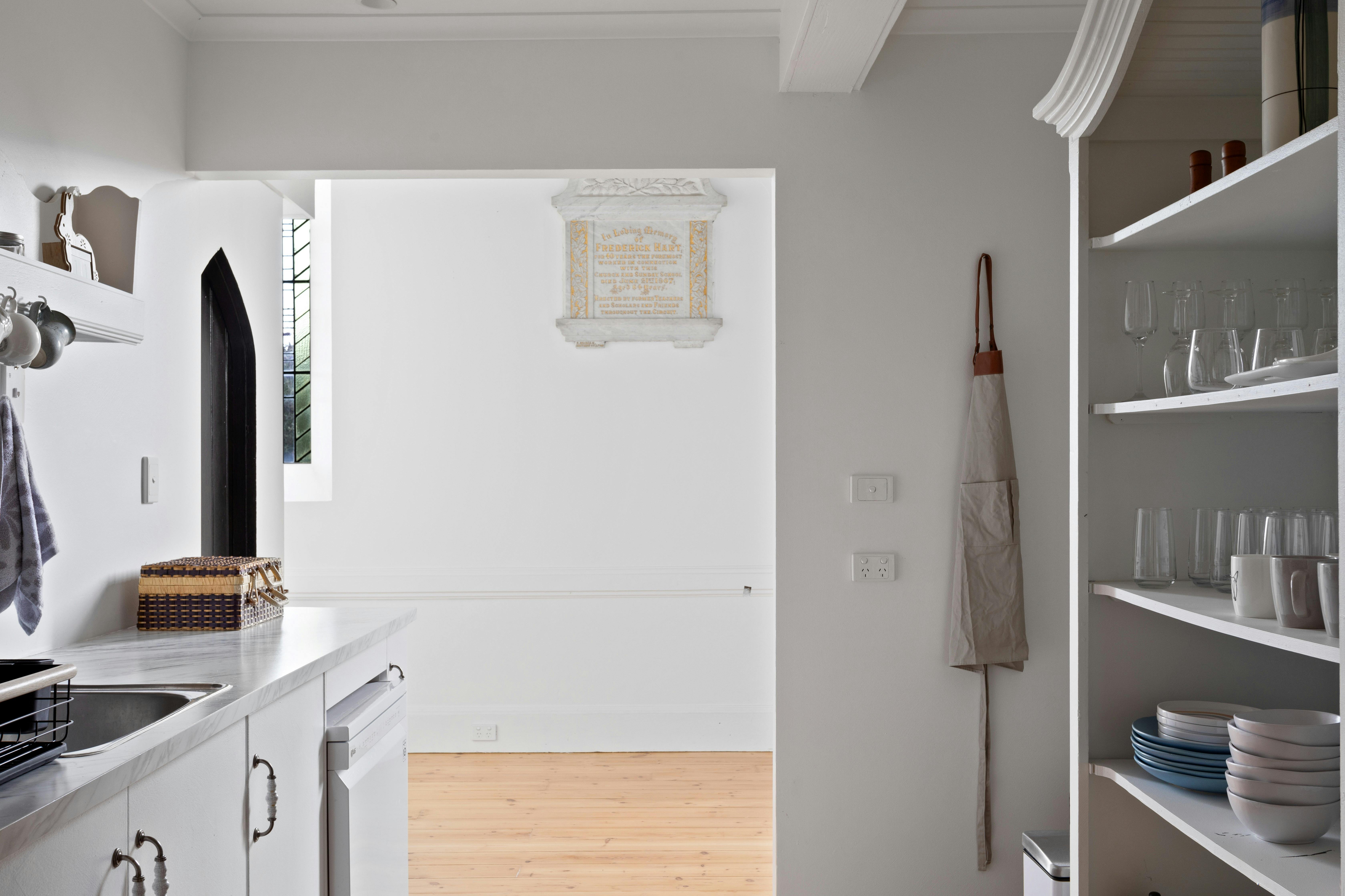 Kitchen shelving with glassware, sink, apron and a commemorative plaque