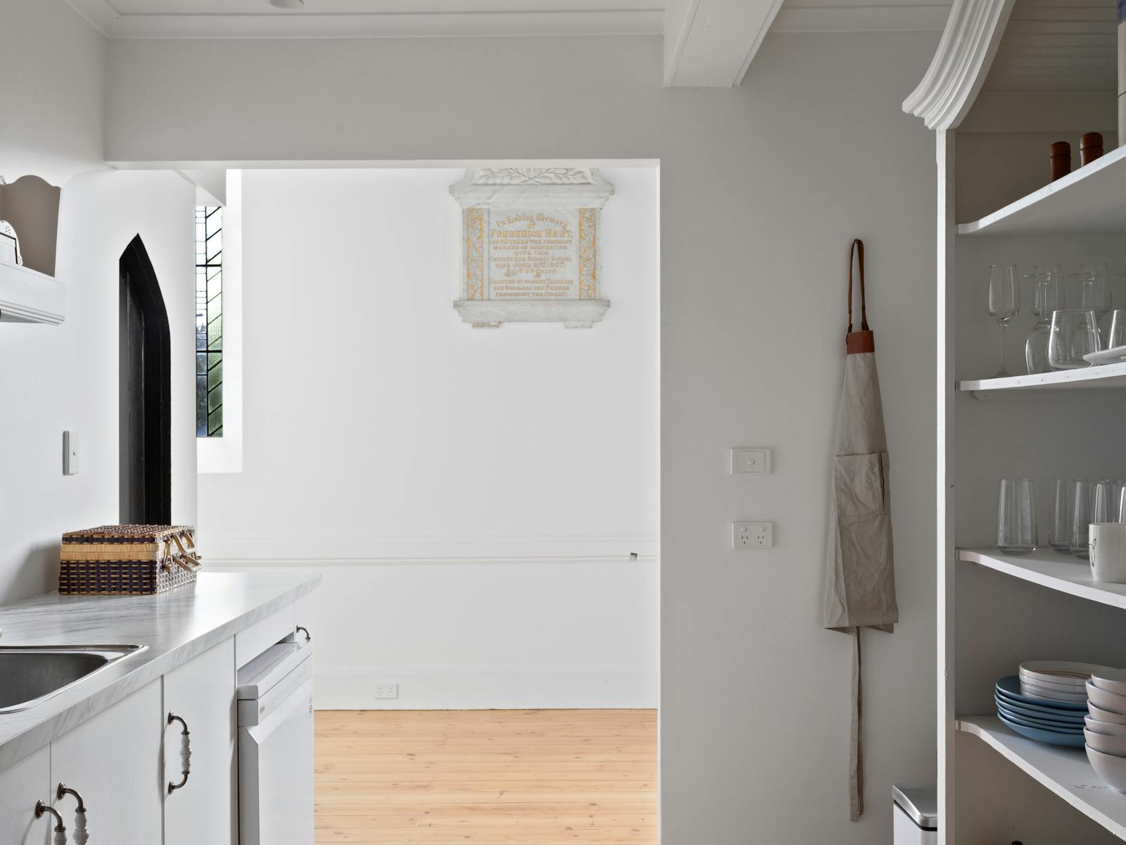 Kitchen shelving with glassware, sink, apron and a commemorative plaque