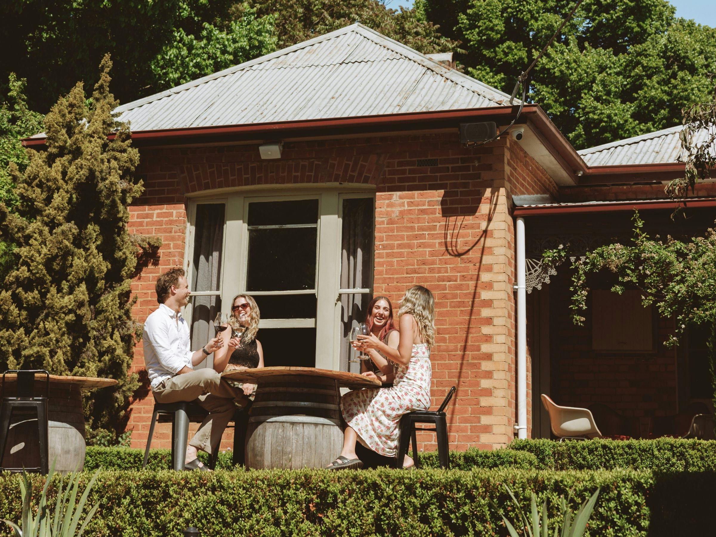 An image of friends sitting around a wine barrel in the sun on the front lawns of Elm Dining