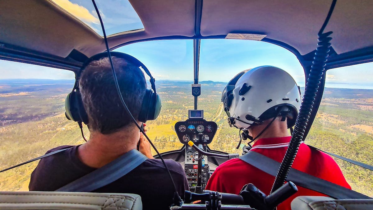 Photo from back seat of helicopter looking out and over pilot and passenger