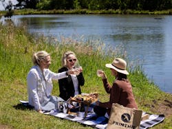 Printhie Wines Picnic Experience with three women sitting on a rug by the lake