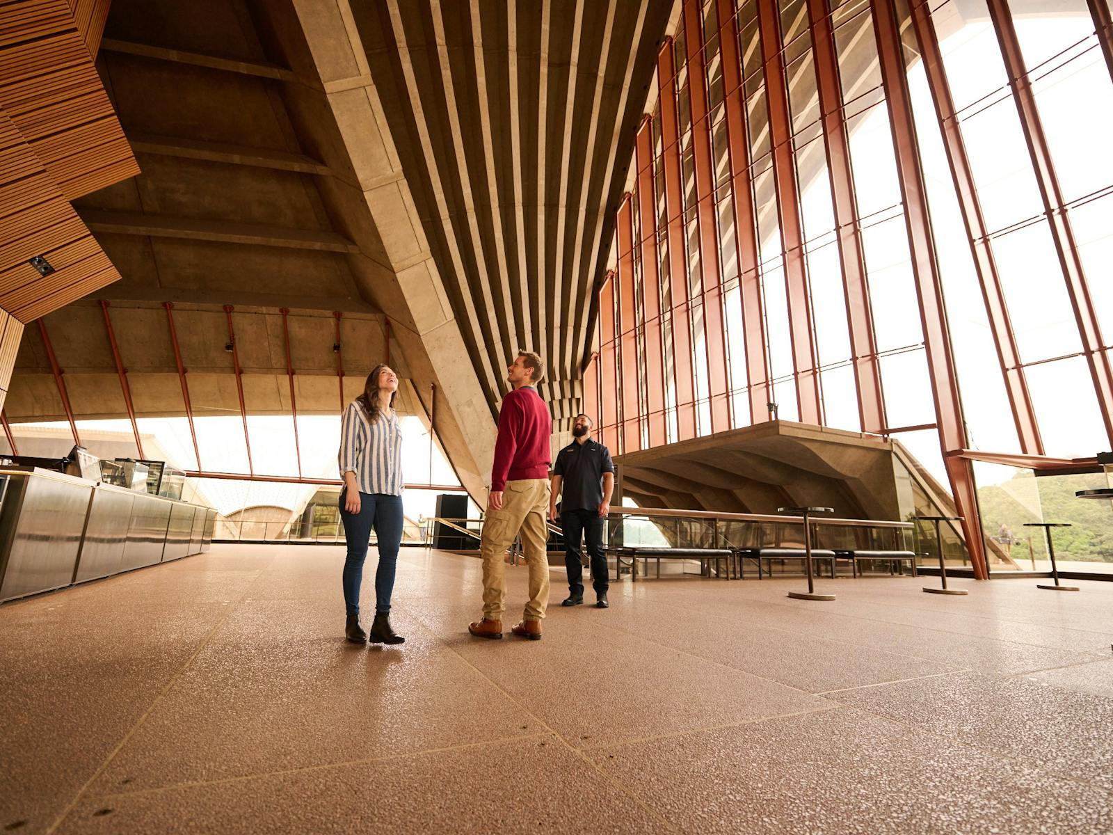 Tour guide, a man and a woman looking up to the cathedral ceiling of the Concert Hall Southern Foyer