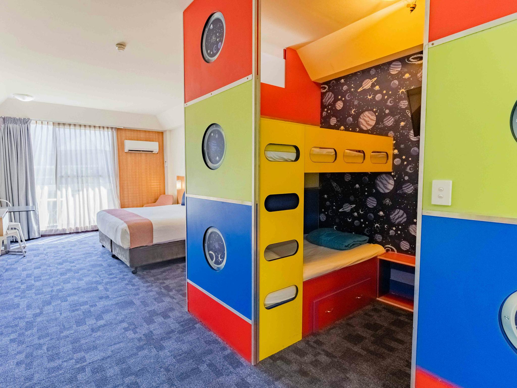A room with one queen bed and a set of colourful bunks A room with one queen bed and a set of colourful bunks