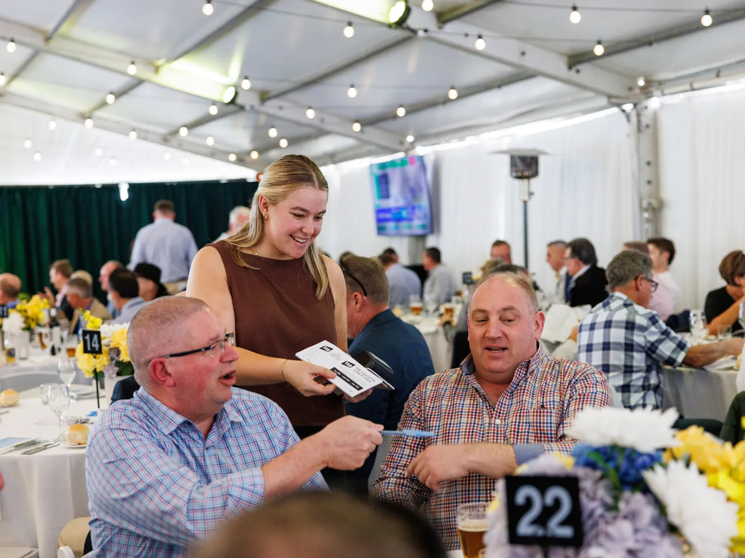 young lady handing over raffle ticket booklet to  2 gentleman