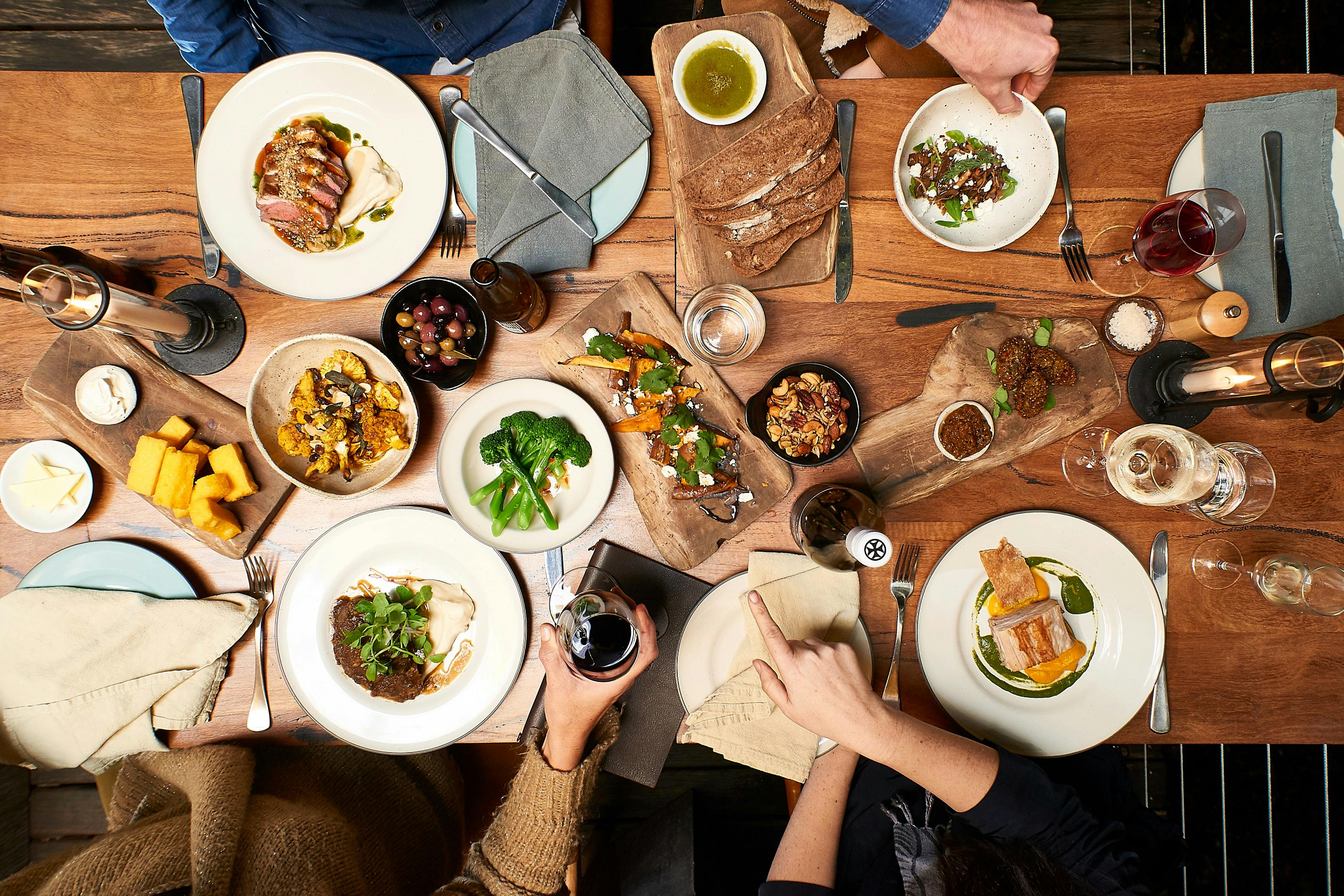 Aerial image of a dining table laden with food and guests hands serving each other.