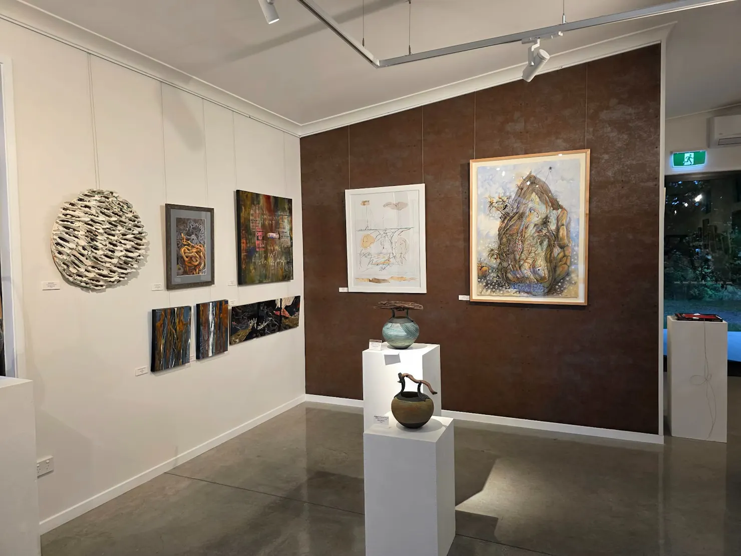 Artworks displayed on copper-look feature wall in art gallery