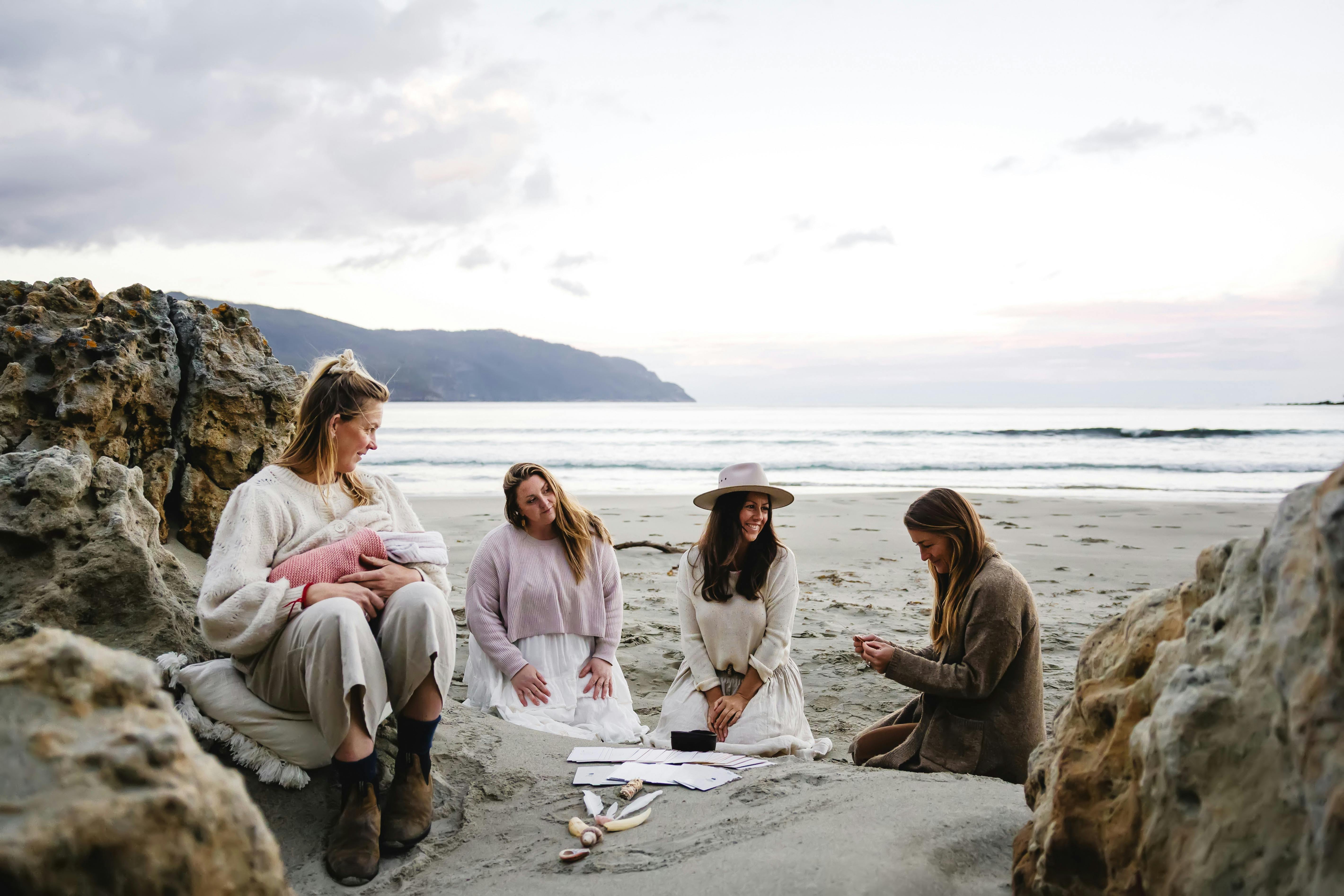 A small group of women sitting on a beach on the Tasman Peninsula, sharing a tarot reading together