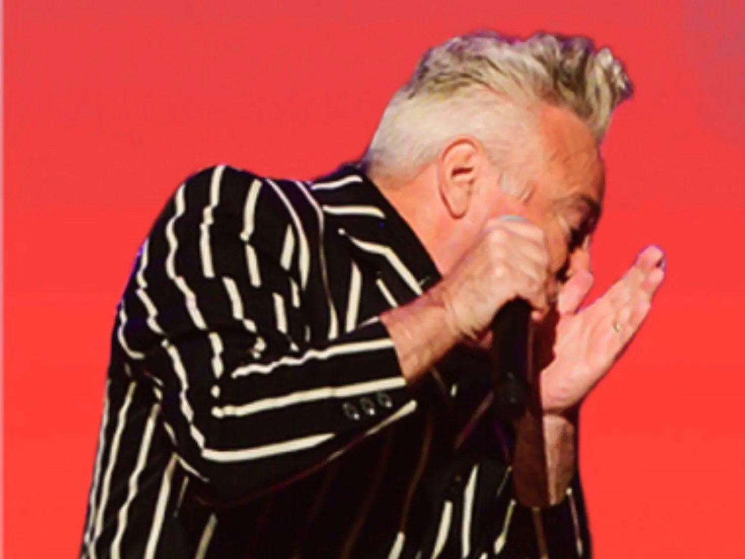 A older guy singing in front of red background.