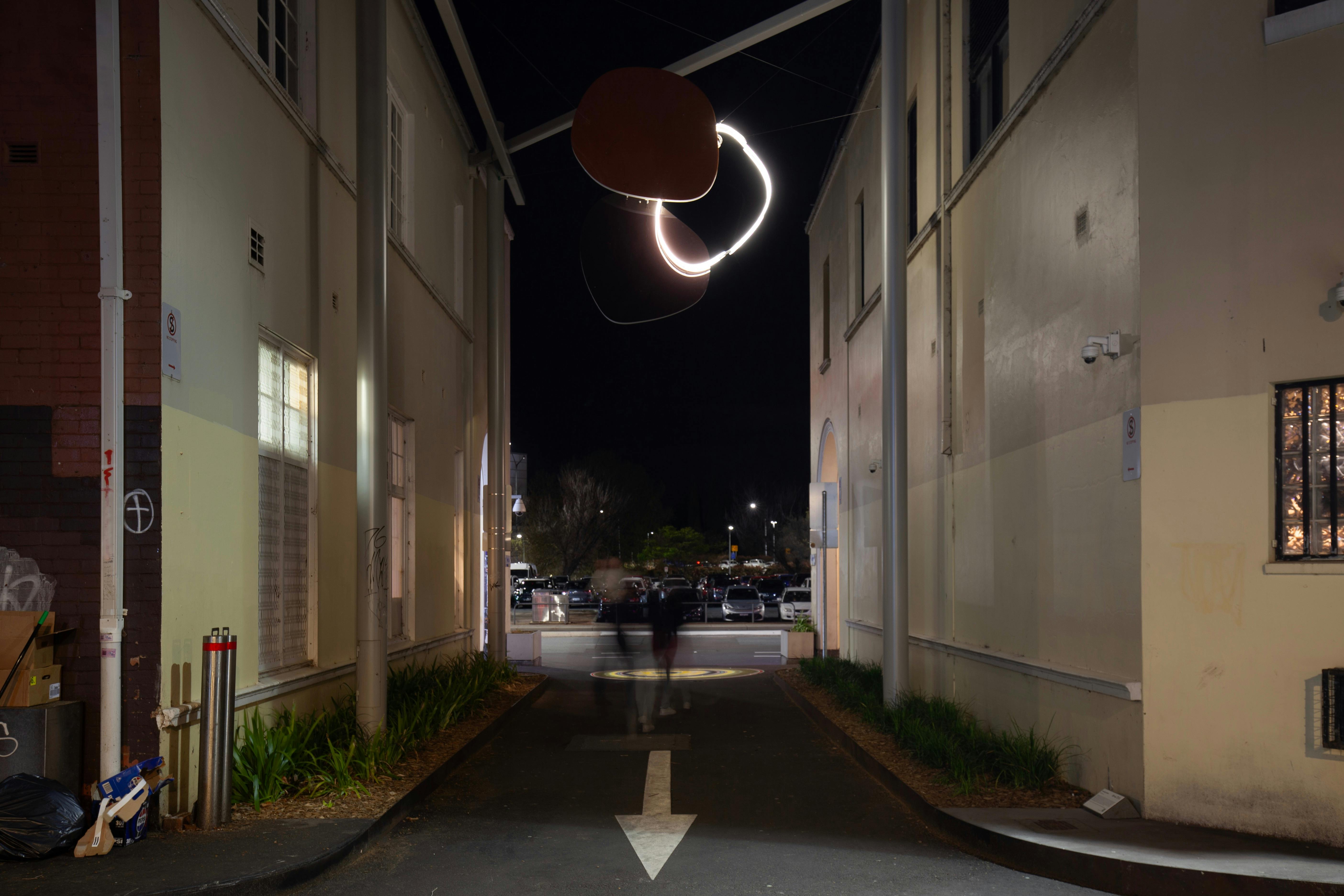A neon sculpture hanging in an alley way at night.