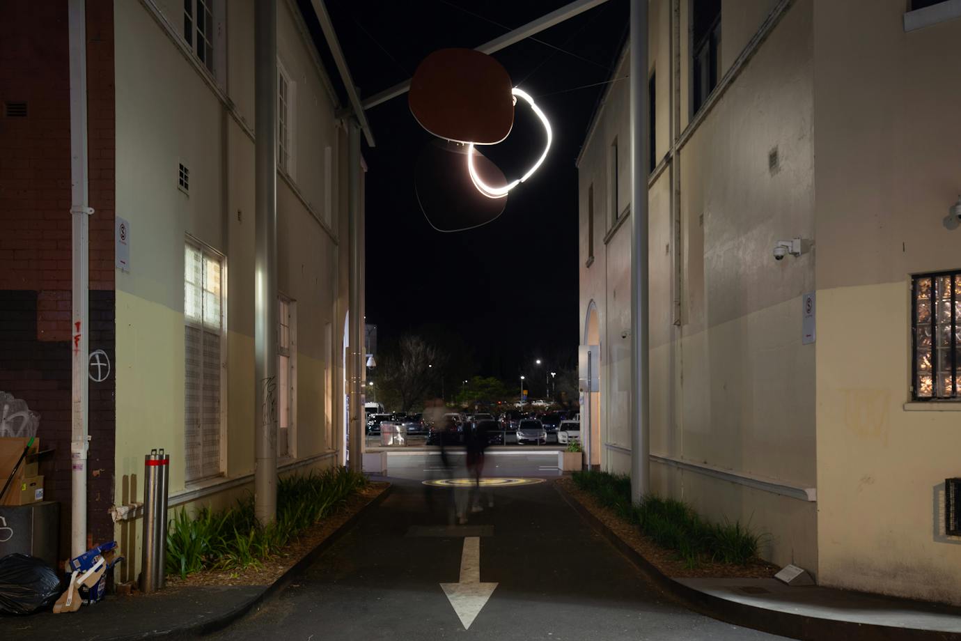 A neon sculpture hanging in an alley way at night.