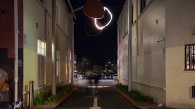 A neon sculpture hanging in an alley way at night.
