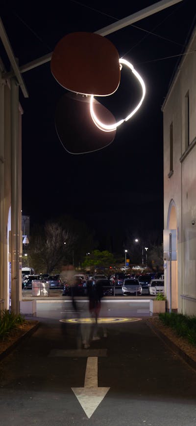 A neon sculpture hanging in an alley way at night.