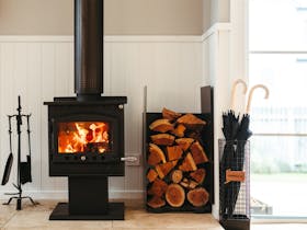 Wood fireplace with stacked firewood and umbrellas inside Tea Tree Retreat accommodation in Robe Sou