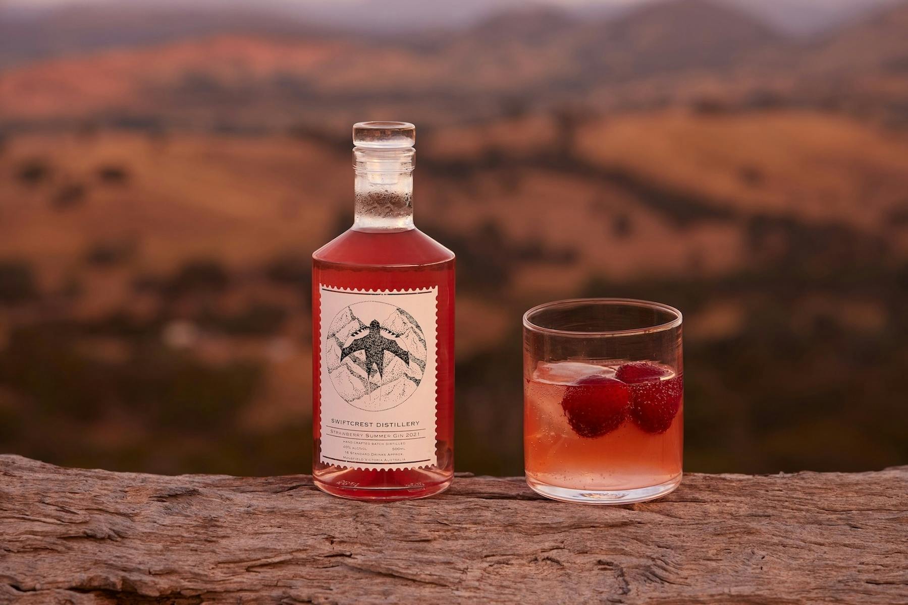 A Swiftcrest Distillery strawberry gin bottle and a cocktail glass with fresh strawberries