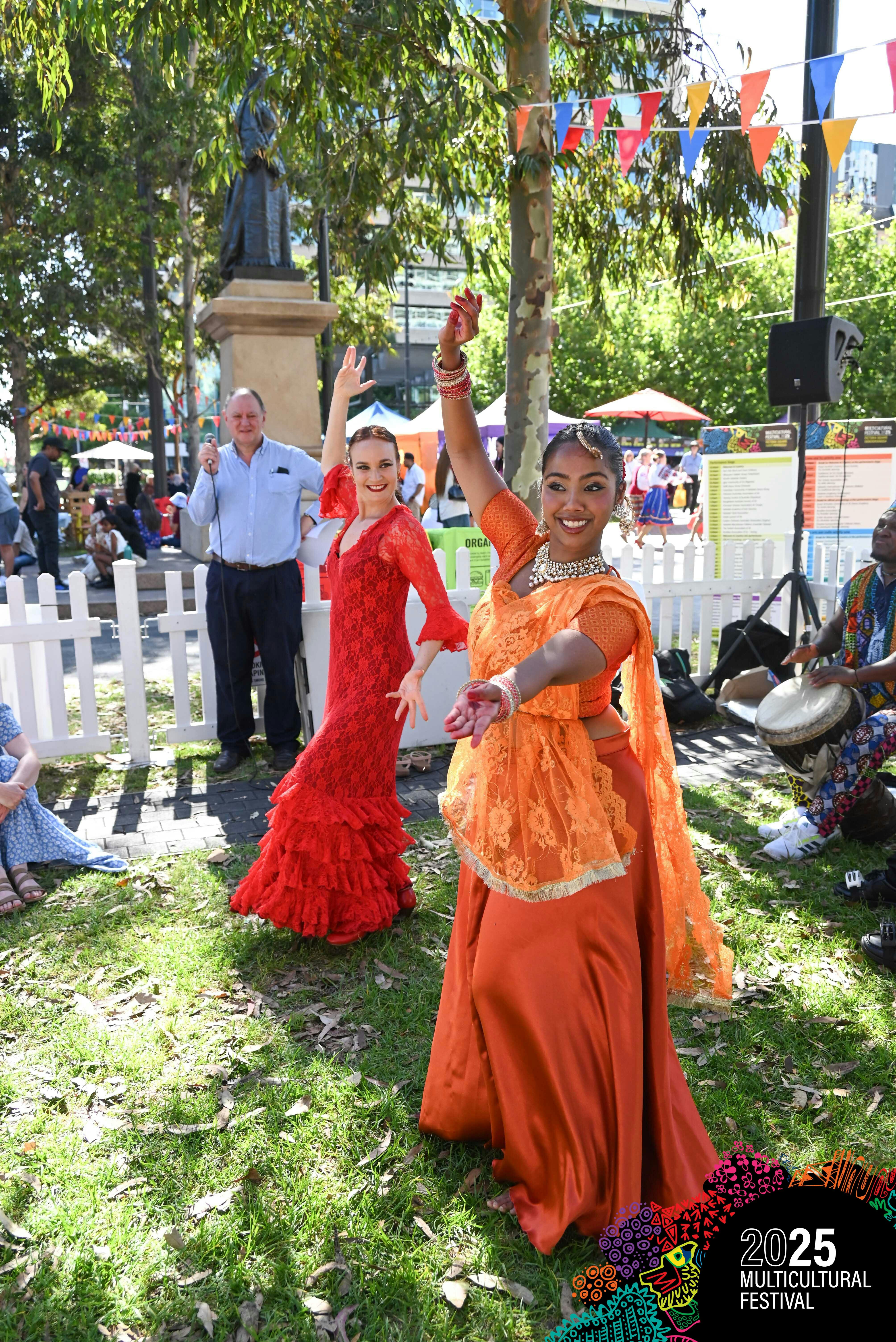 Two dancers in traditional costumes showing dance moves in an open aired space with an MC