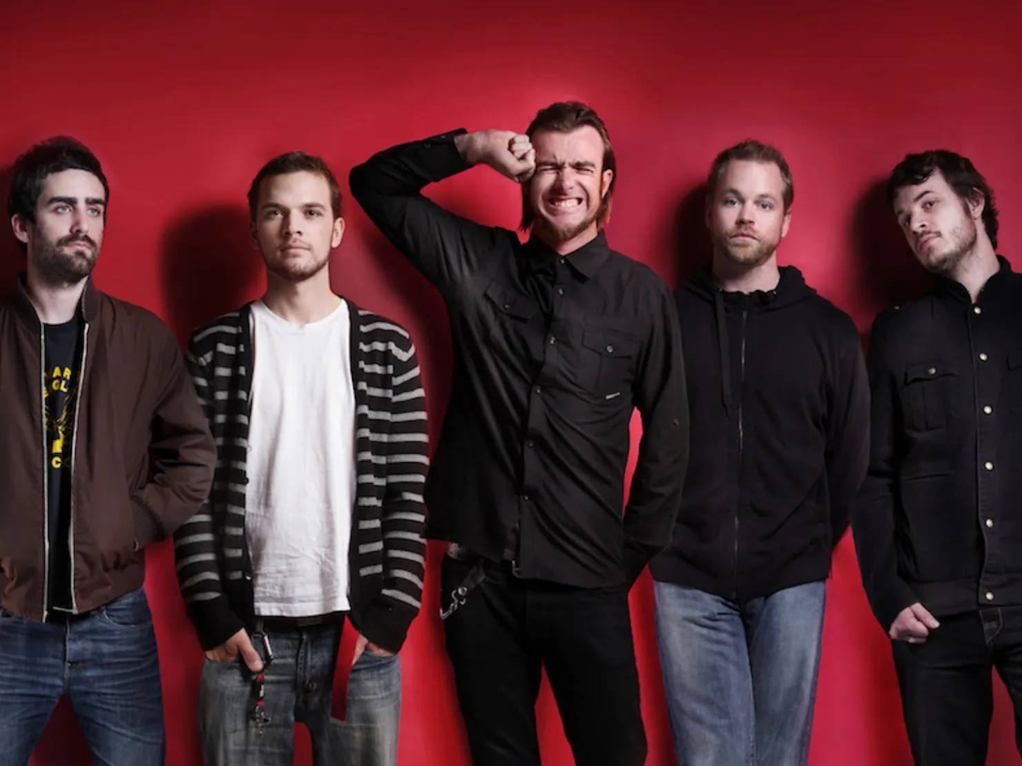 Whole band standing in a line infront of a red wall posing for a photo