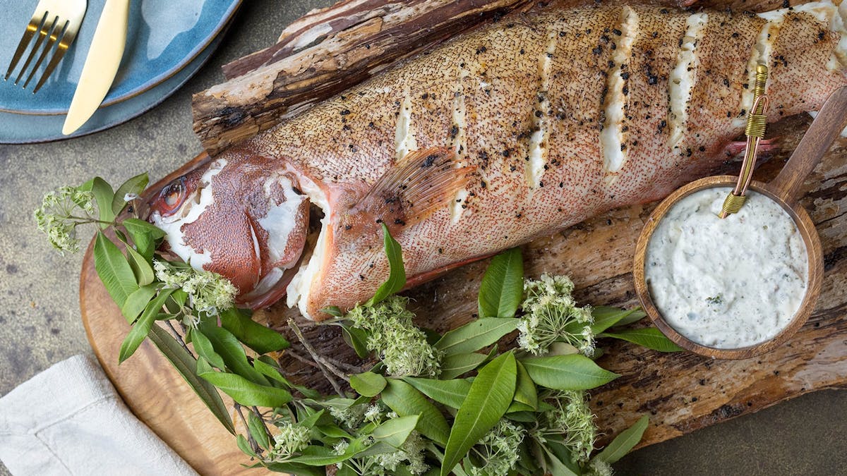 Cooked fish on a wooden chopping board with greens