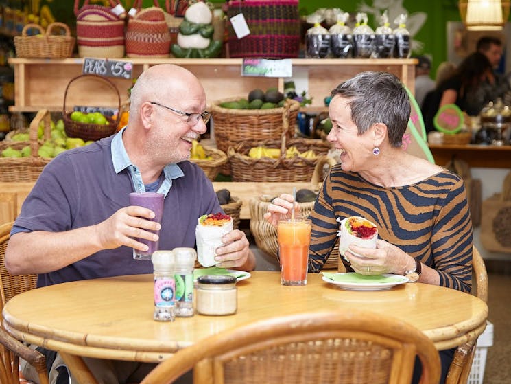 Man and woman sitting at cafe table eating salad wraps with fresh juice and smoothie