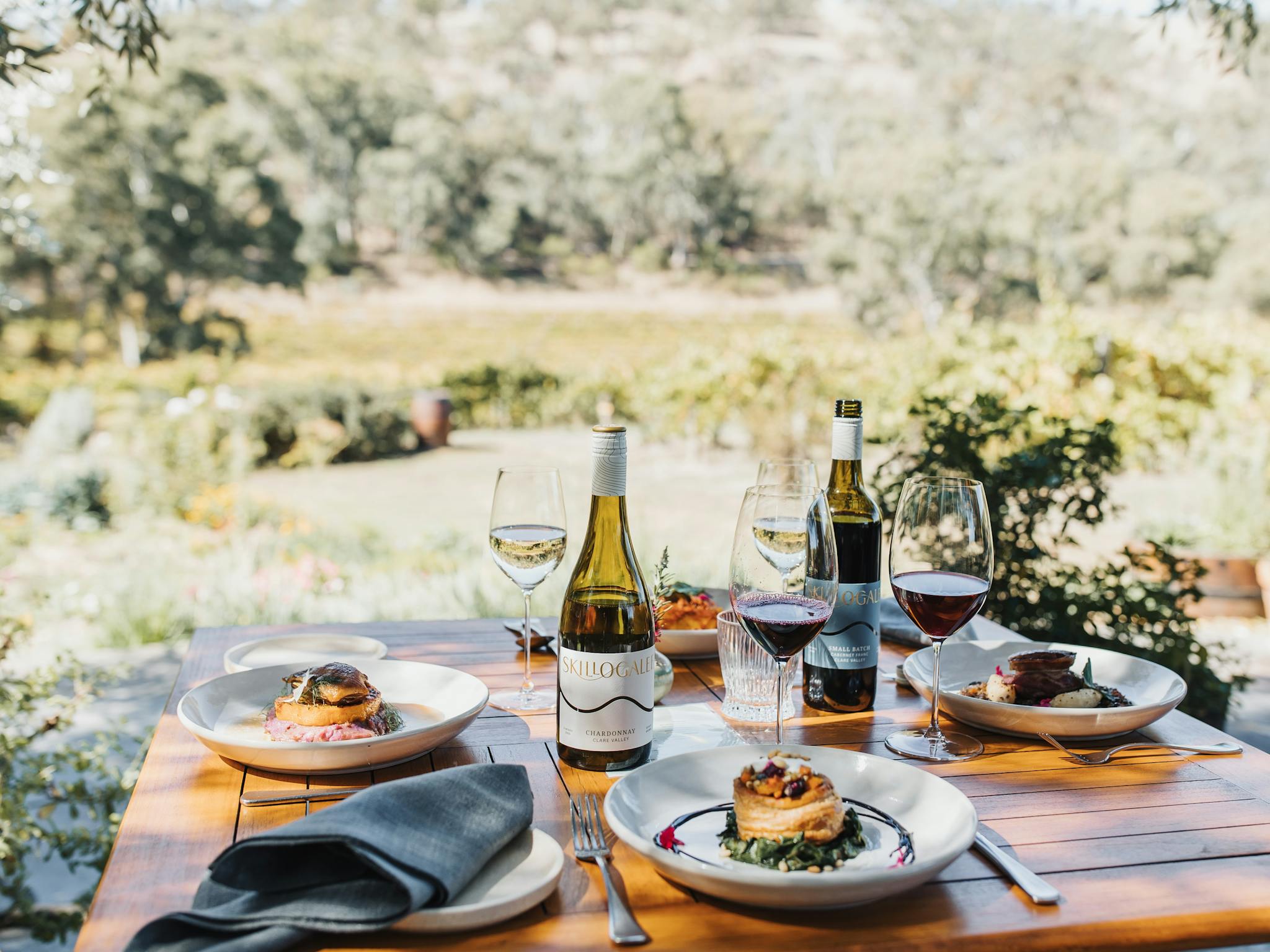 A table set for lunch outside, with the wooded hills and Skillogalee's iconic vineyards behind
