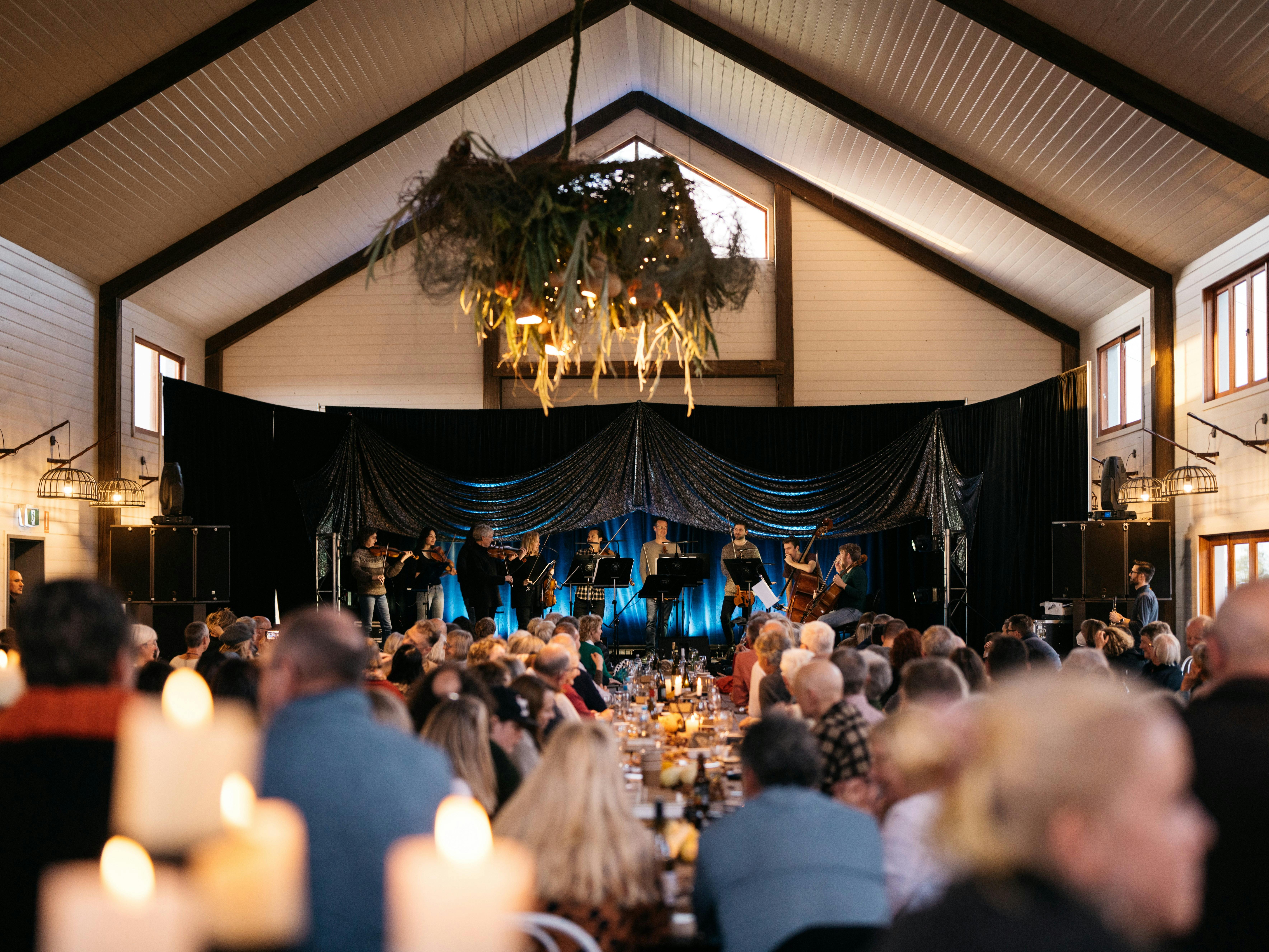 A large room with musicians on a stage and people and candles in the foreground.