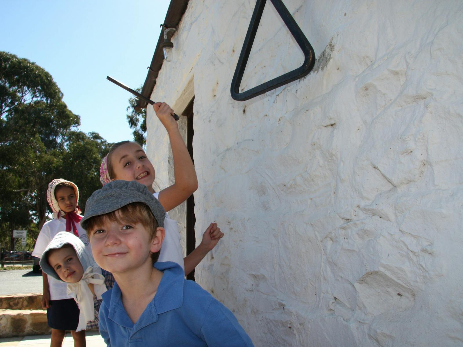Four children in 18th century dress next to a white washed wall