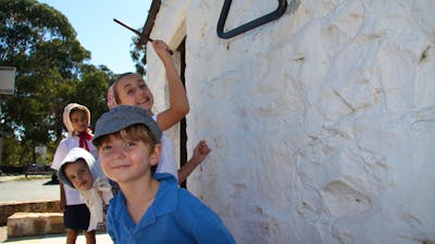 Four children in 18th century dress next to a white washed wall
