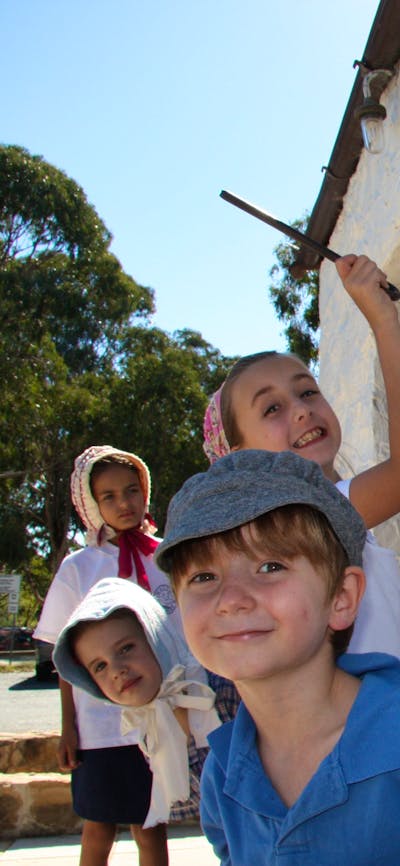 Four children in 18th century dress next to a white washed wall
