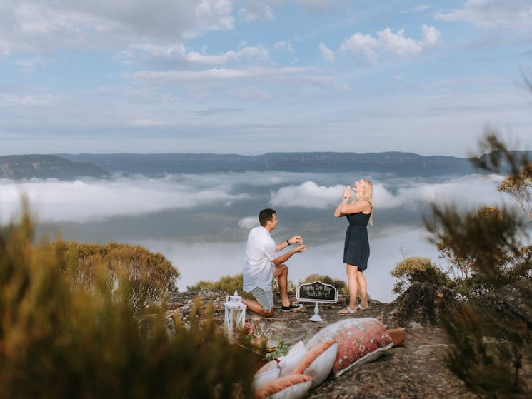 A picture containing cloud, outdoor, sky, a person kneeling proposing to another person