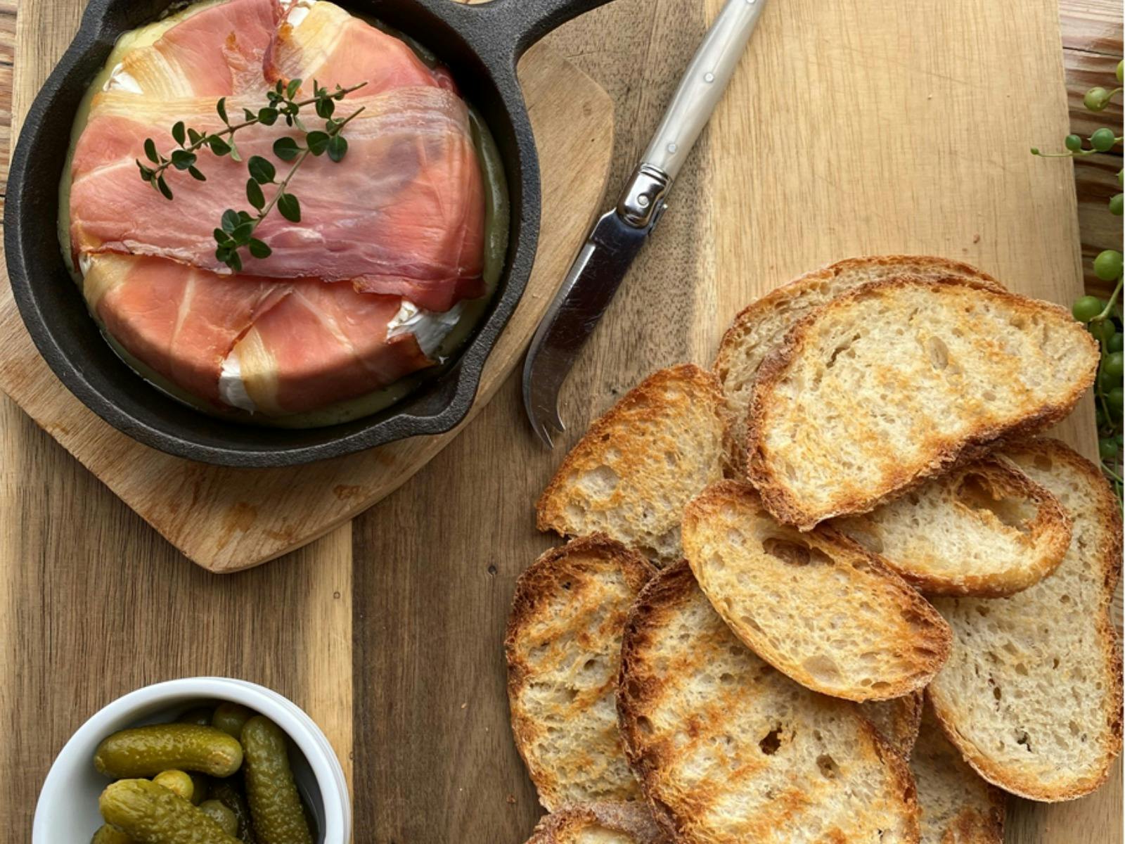 Image of baked camembert wrapped in proiscutto with grilled warm bread