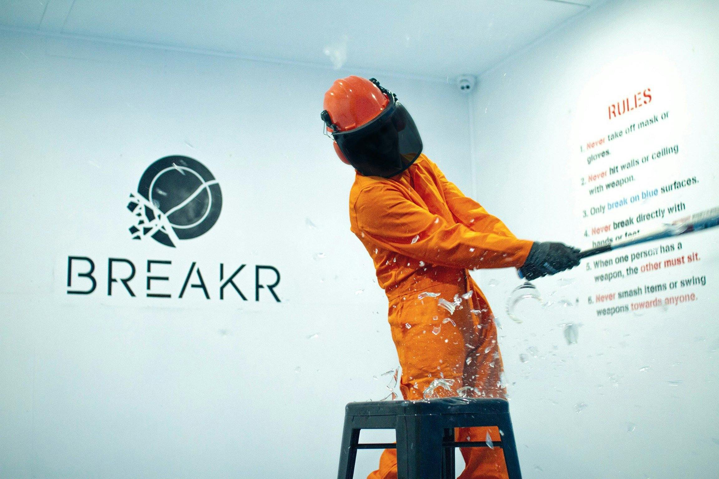 Someone in protective gear, smashing glass with a bat