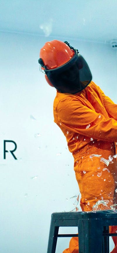 Someone in protective gear, smashing glass with a bat