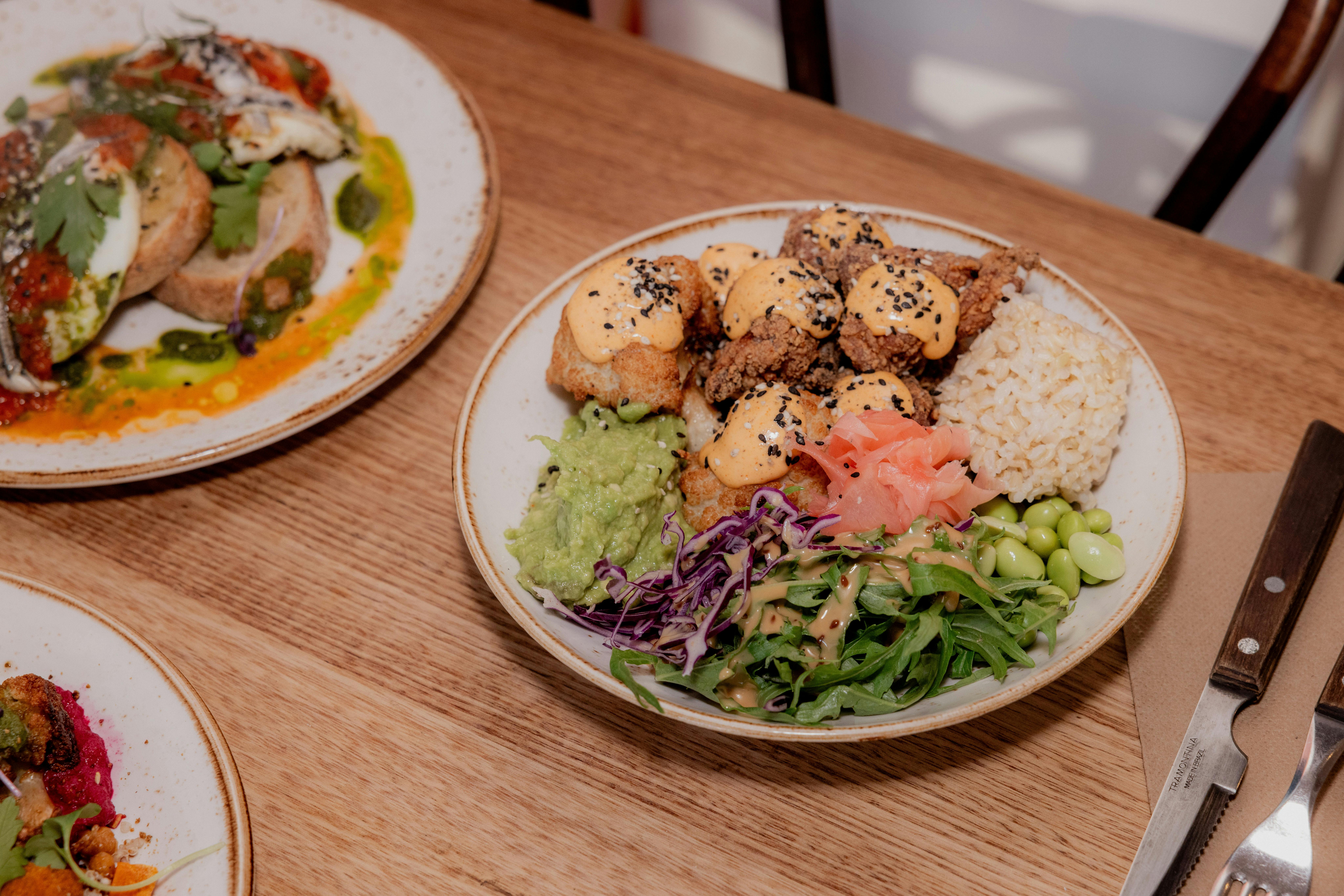 food sitting on cafe table, salad including fried chicken, brown rice, avocado, rainbow slaw