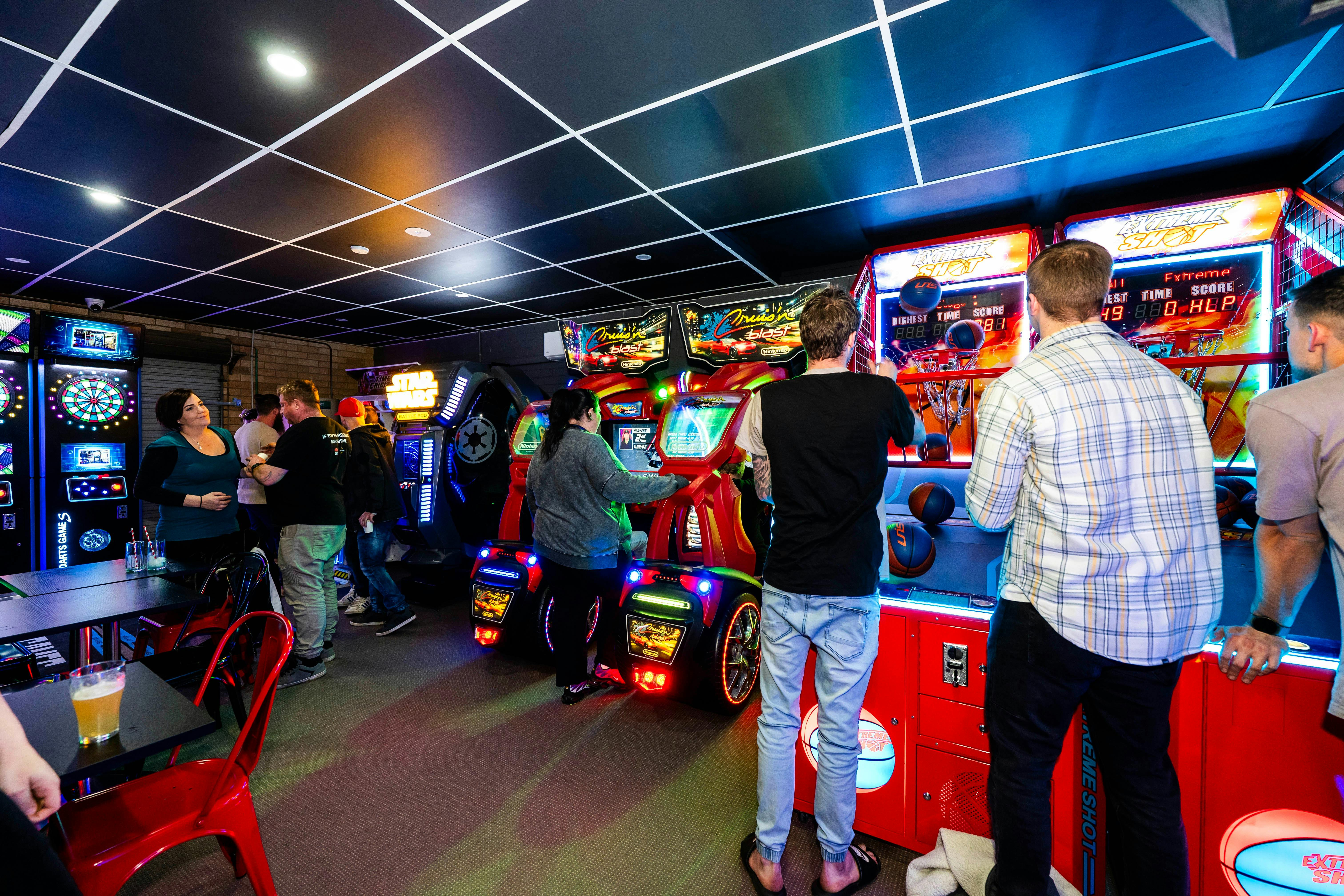 Group of people playing various arcade machines under the colorful neon ceiling lights