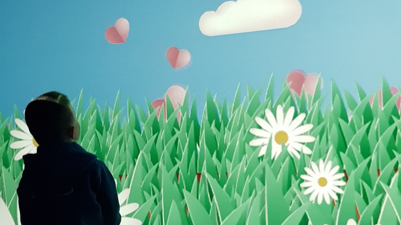 Young child moving his body to interact with a large-format digital game projected onto a wall.