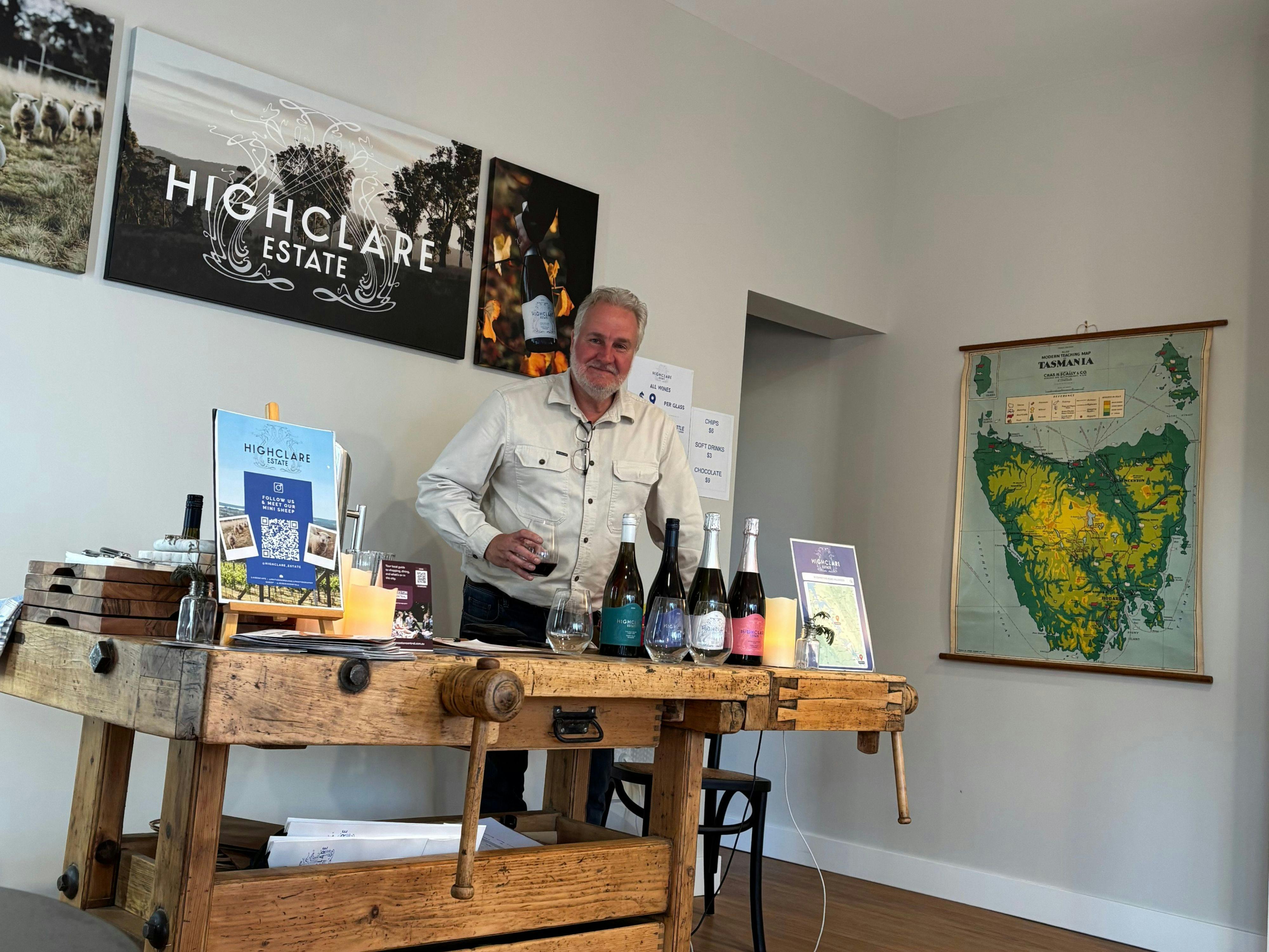 Wine bottles arranged on antique wood working bench, man standing, map of Tasmania on rear wall