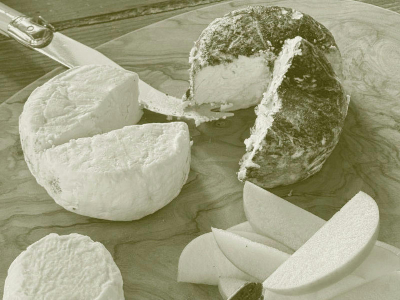 Soft cheese with wedge missing on wood board and silver knife. Slices of pear on side.