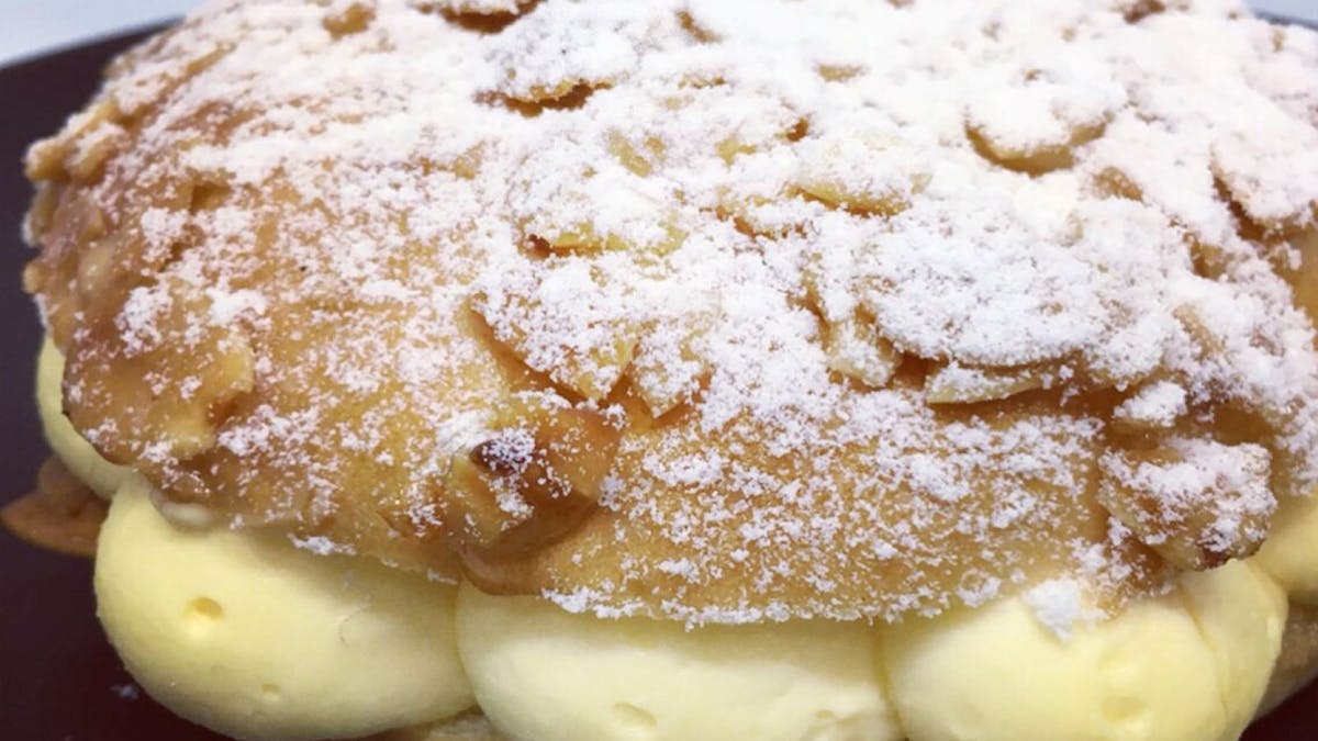 A Beesting pastry filled with fresh cream and topped with almonds and dusted with icing sugar