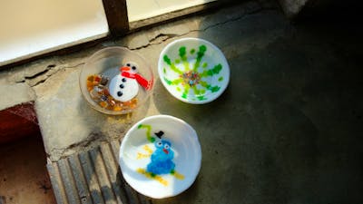 3 glass bowls made through kiln forming, two with snowman deisgns, and one with a colourfull snowfla