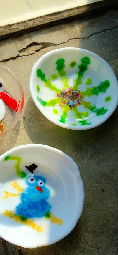 3 glass bowls made through kiln forming, two with snowman deisgns, and one with a colourfull snowfla
